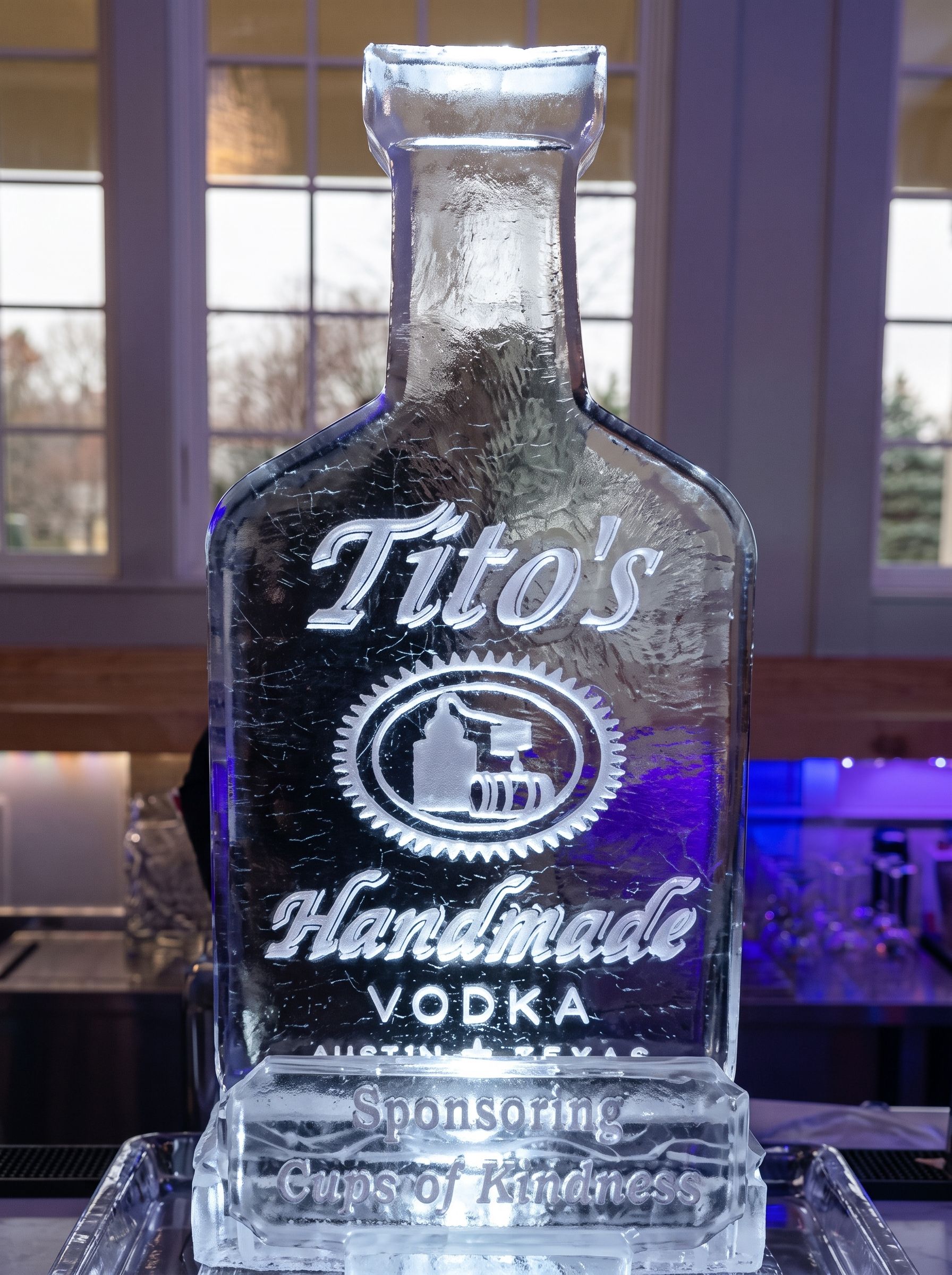 Tito’s Handmade Vodka bottle with frosted glass on a counter before a purple-lit window