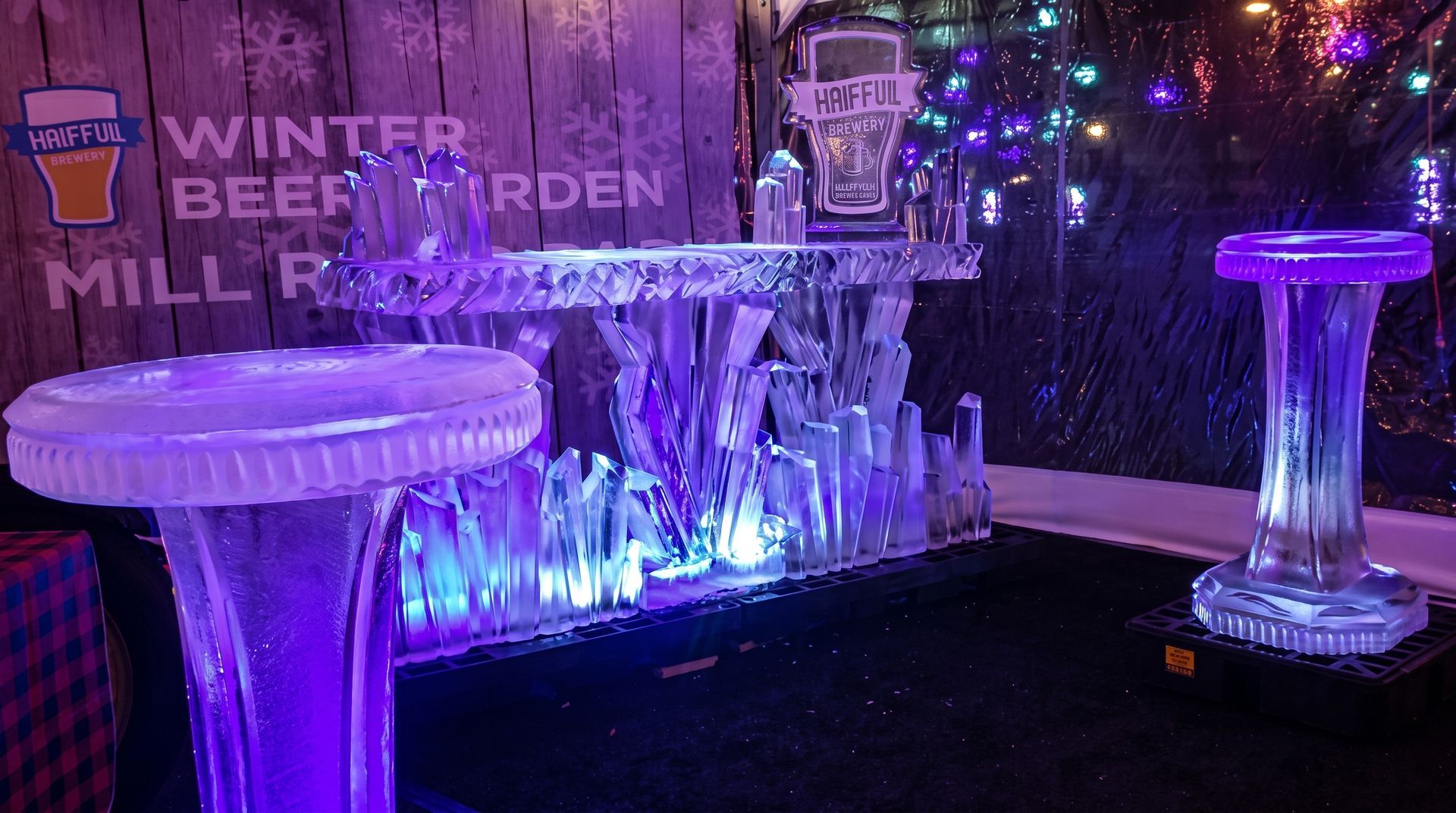 Purple-lit ice sculptures in a winter beer garden with a “Mill River” sign