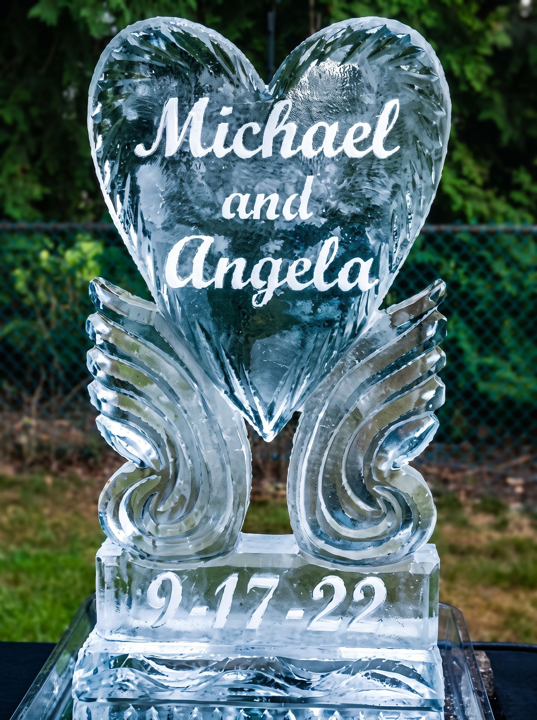 Heart-shaped ice sculpture engraved “Michael and Angela” with the date “9.17.22” in an outdoor setting