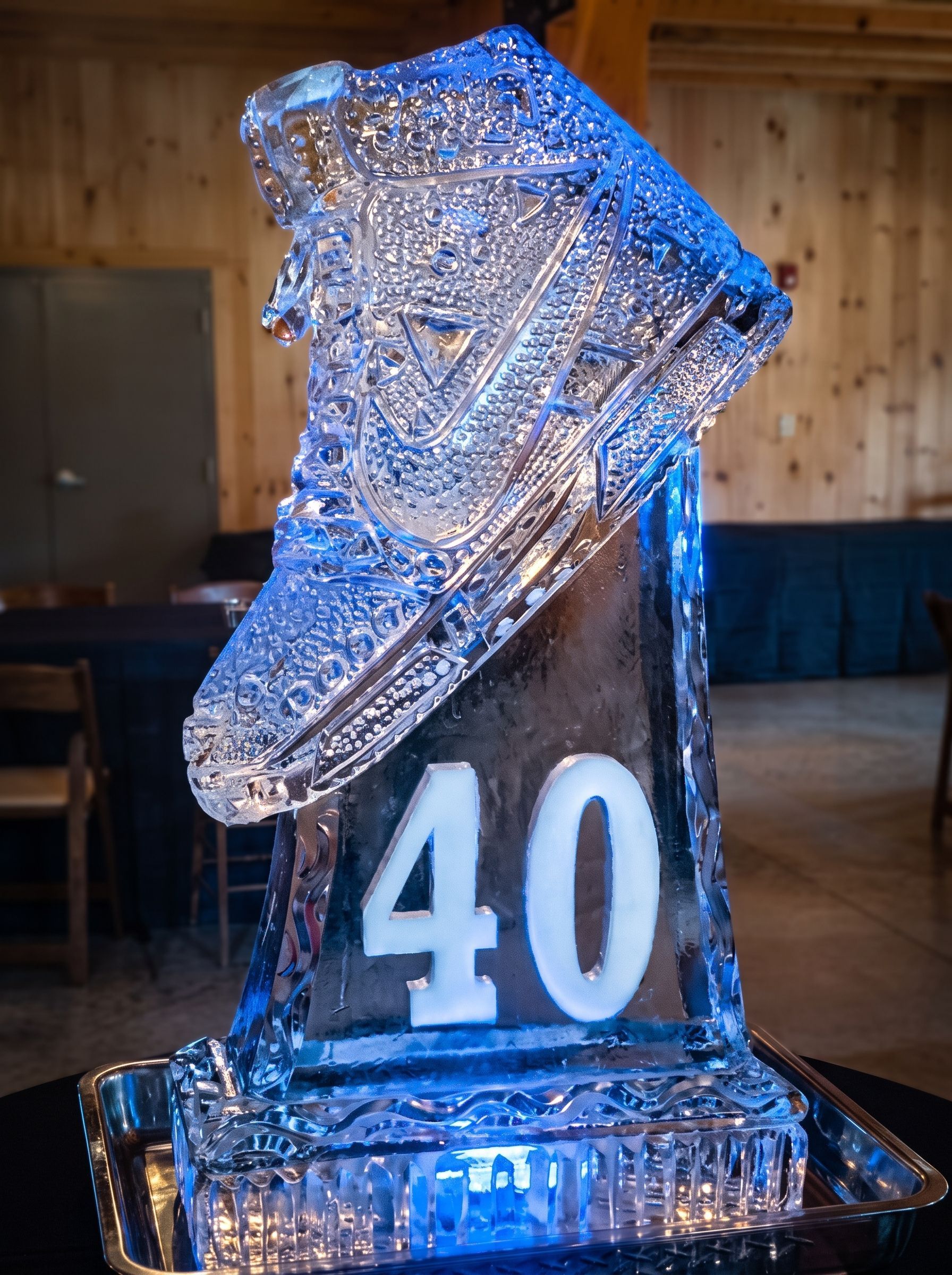 Ice sculpture of a shoe on a black pedestal with the number 40, lit blue indoors