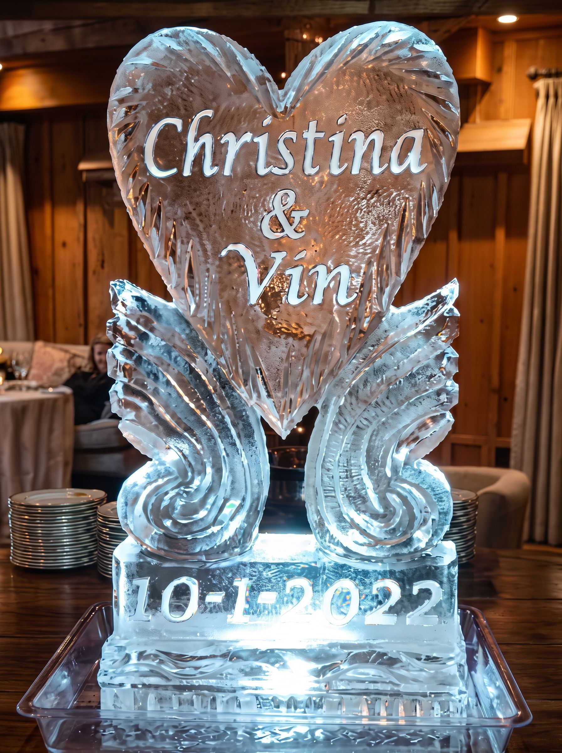 Clear ice sculpture with “Christina & Vin” and “10-1-2022” lit from below on a table
