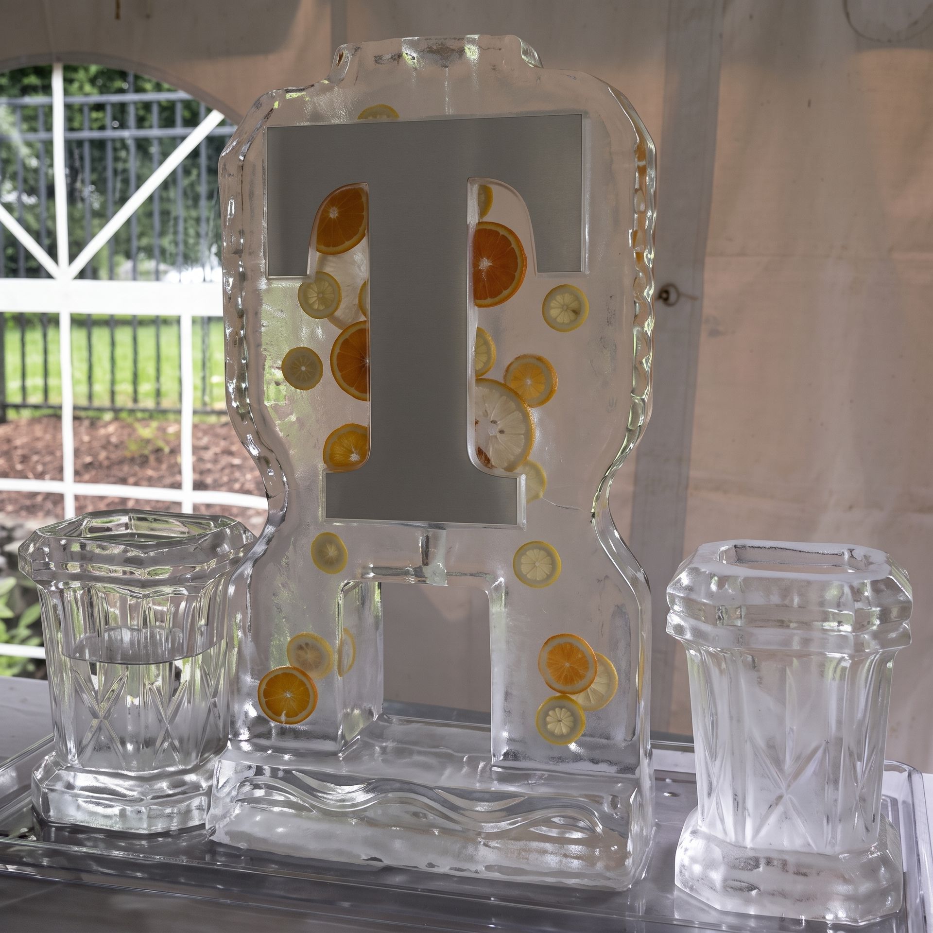 Clear decorative glass pitcher with citrus slices beside two matching glasses on a table.