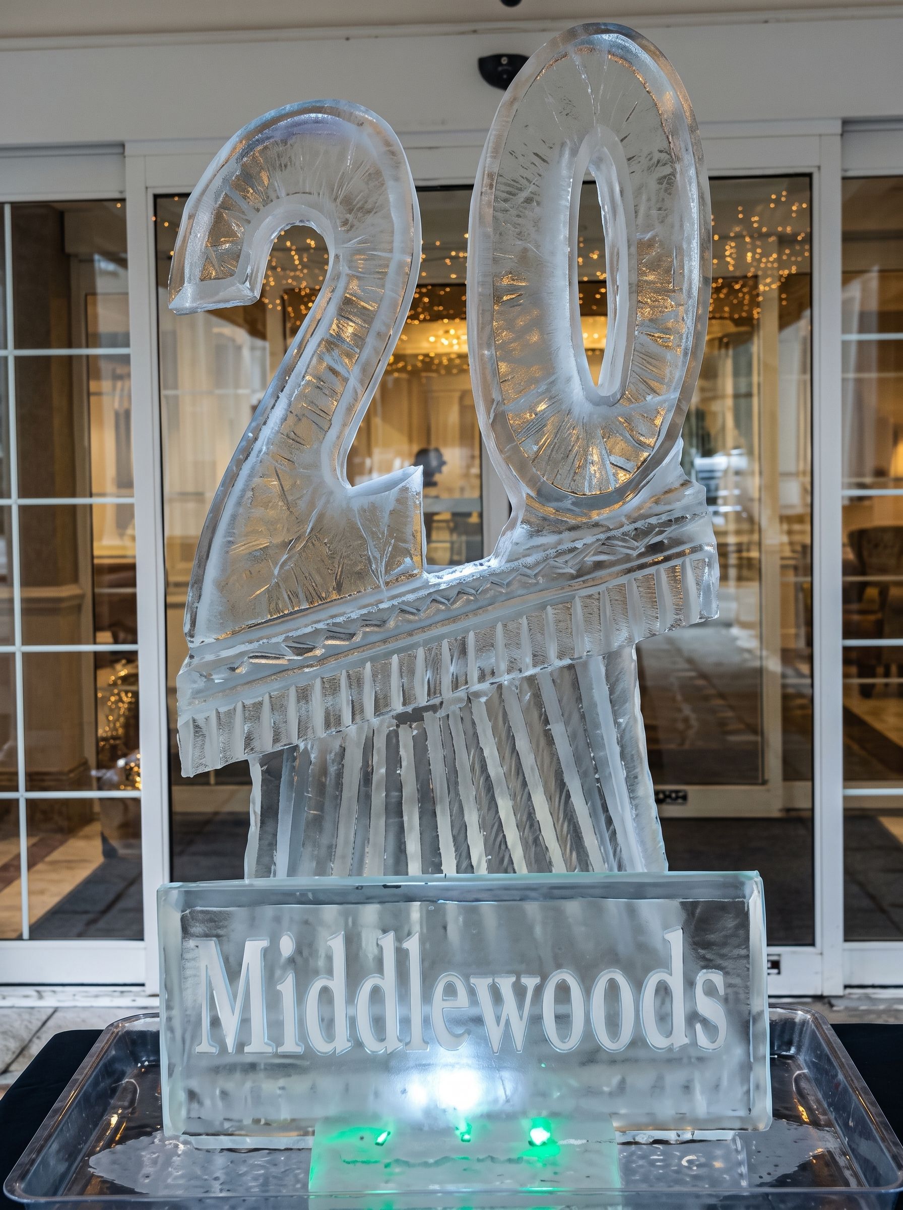 Ice sculpture reading “20 Middlewoods” in front of glass doors, lit from below.
