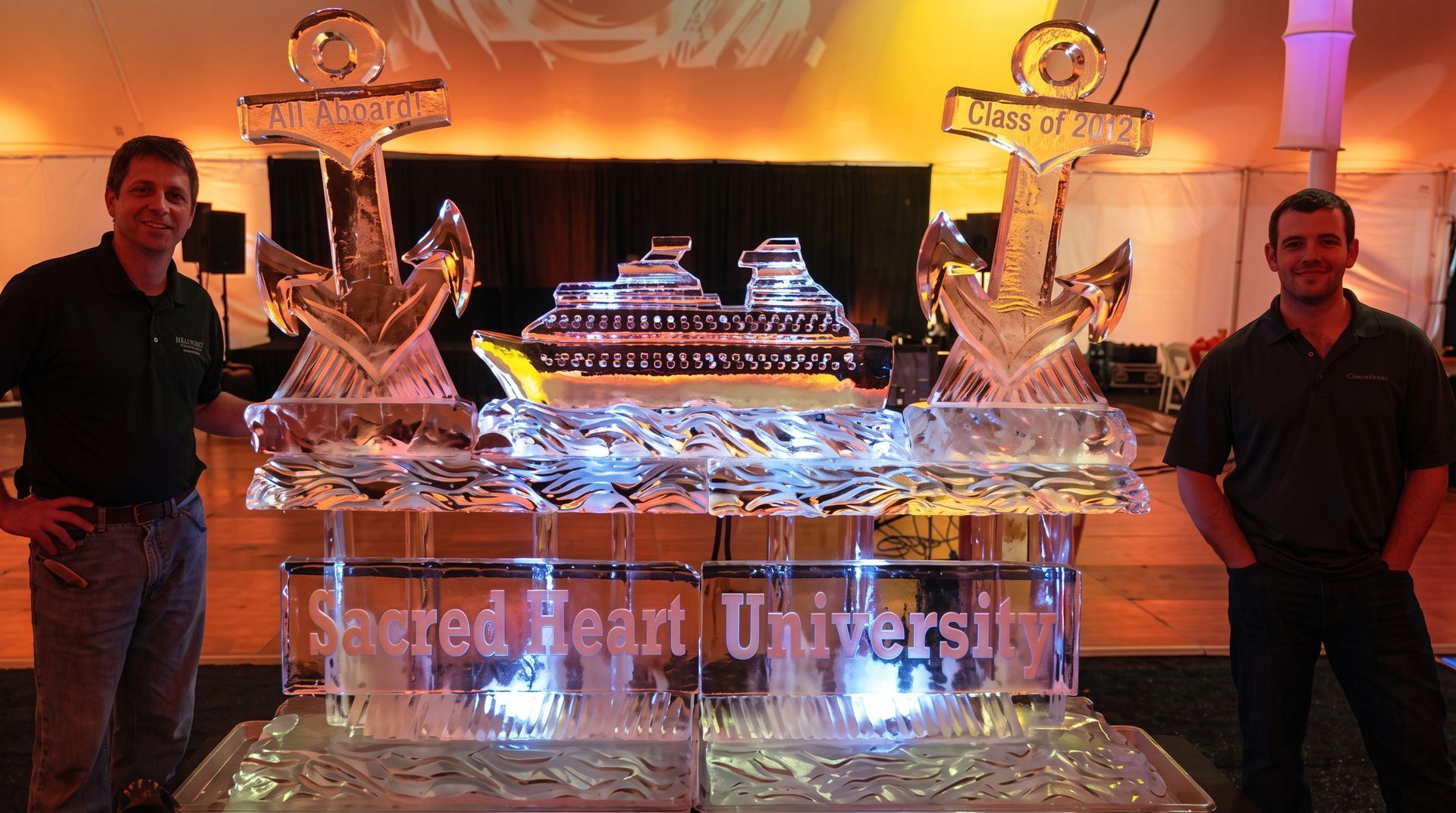 Two men standing beside a lit crystal cruise ship display at a university event