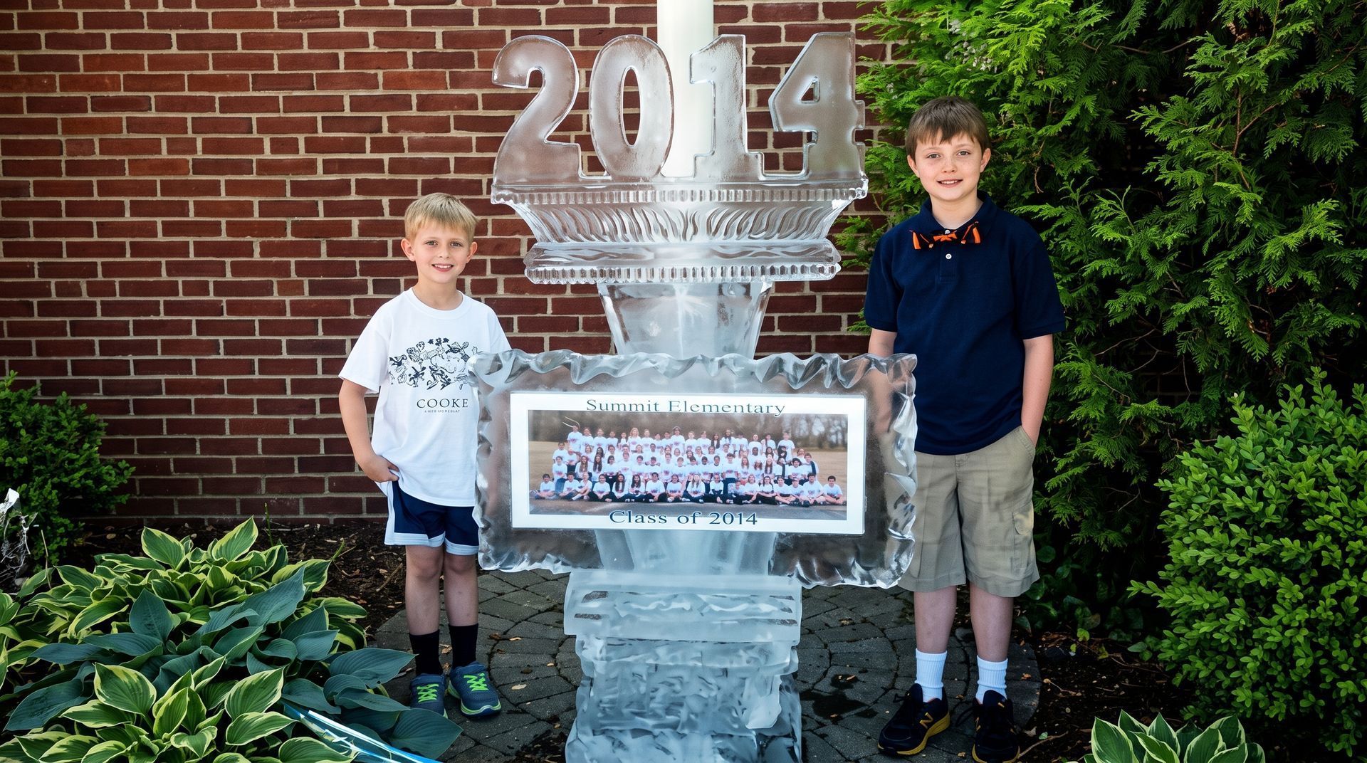 Two boys standing beside a large 2014 sign and display against a brick wall
