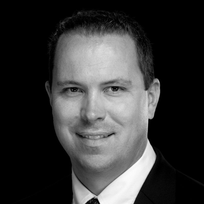 Man in a suit, smiling, headshot with a black background.
