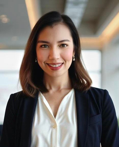 Woman in a blazer smiles, posing in a well-lit office.