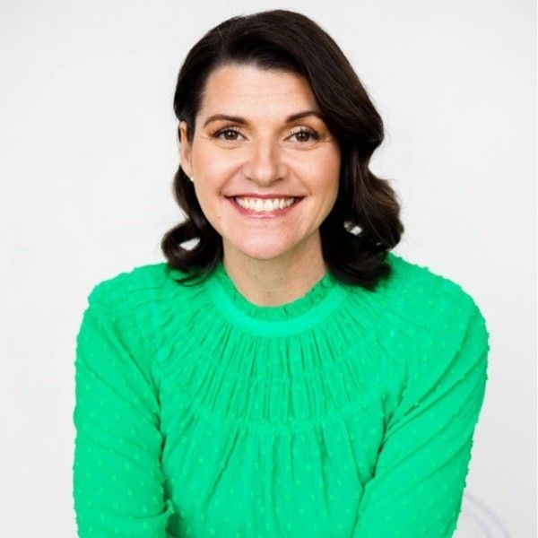 Woman with dark hair smiles, wearing a green textured top, against a white background.