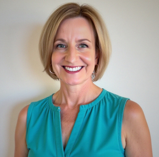 Woman with short blonde hair smiles, wearing a turquoise top.