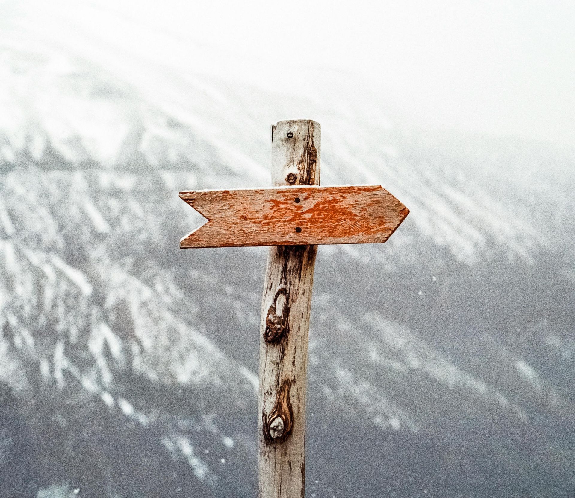 Wooden directional signpost pointing right, set against a blurred snowy mountain background.