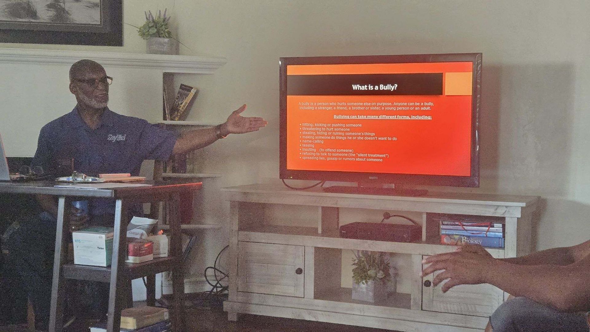 Person presenting beside a TV displaying a red slide in a living room setting