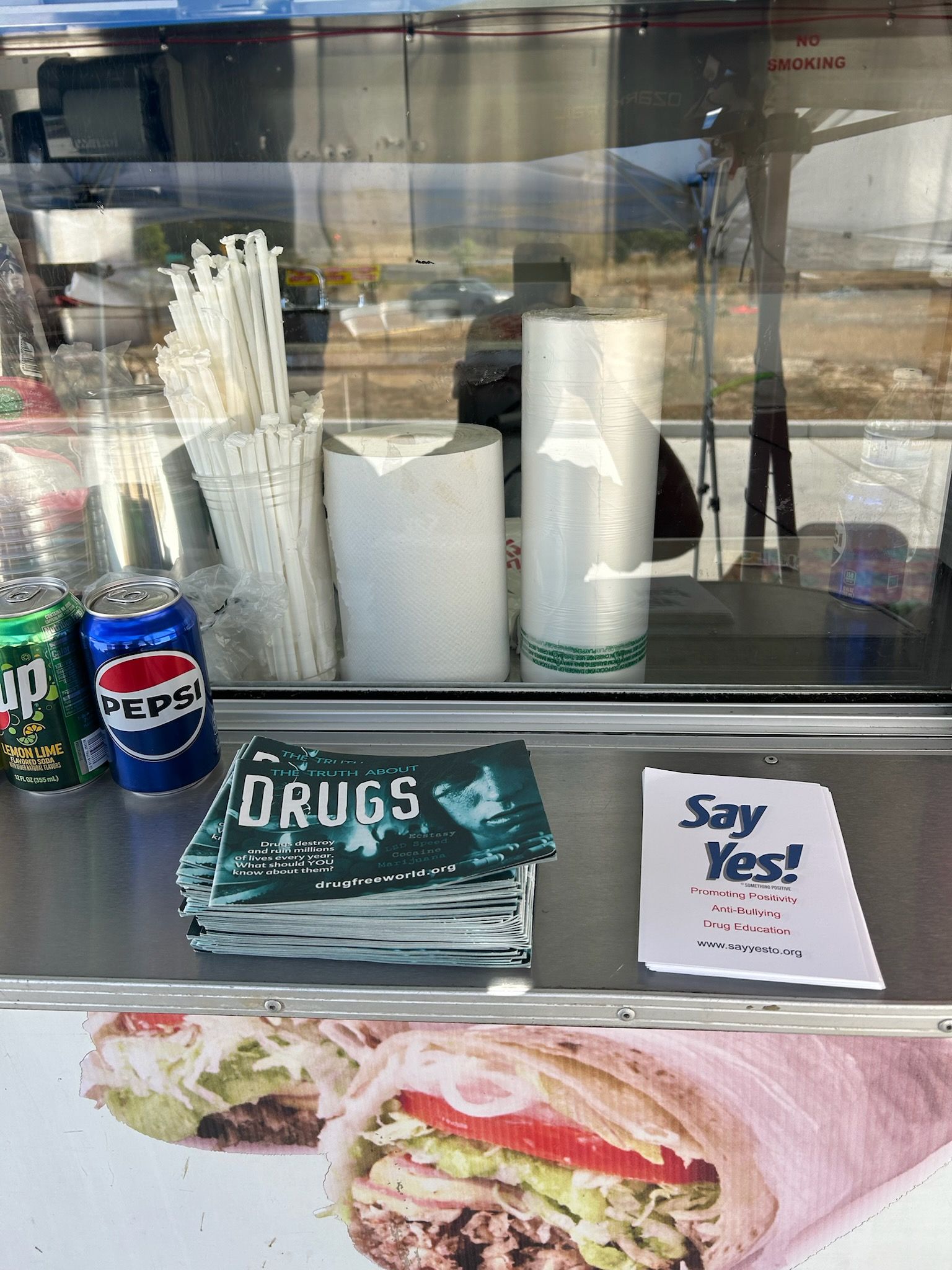 Café counter with cups, napkins, drink cans, and a “Say Yes!” sign beside a burrito photo.