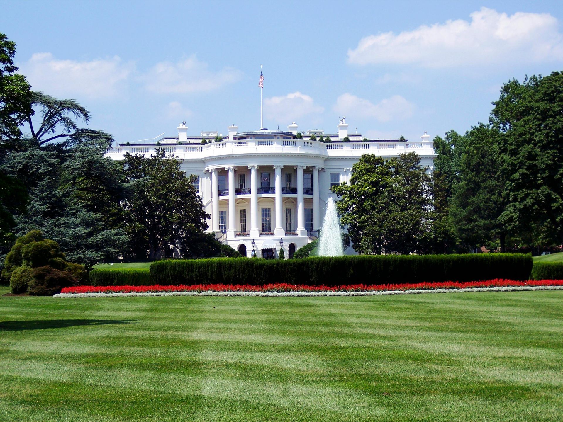 White House, Washington D.C., with green lawn, red flowers, and blue sky.