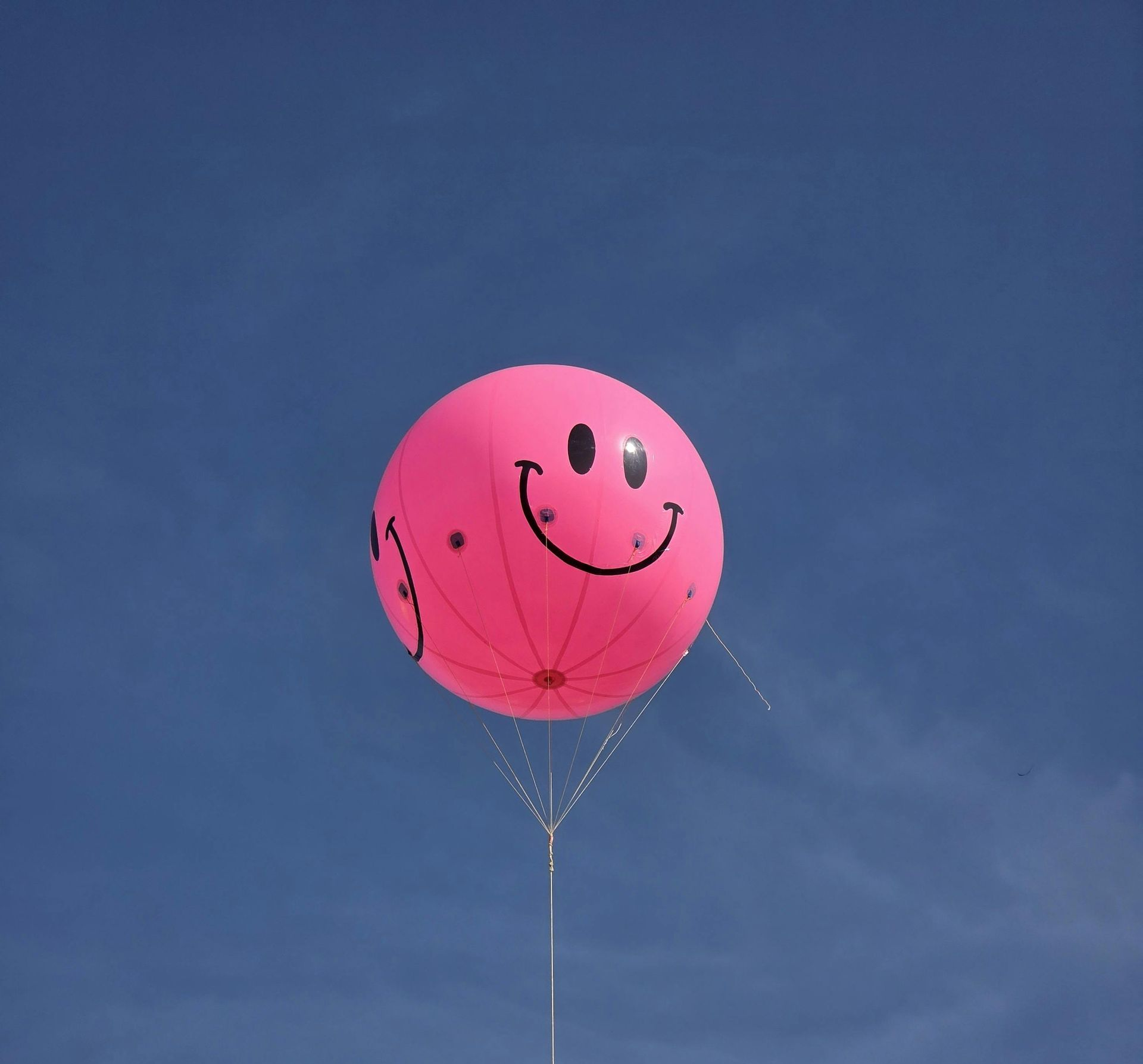Pink smiley face balloon floating in a blue sky.