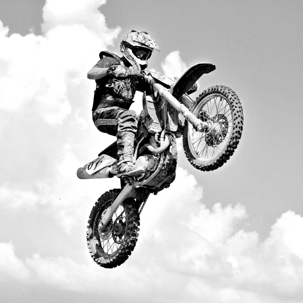 Motocross rider in mid-air, performing a wheelie against a cloudy sky.