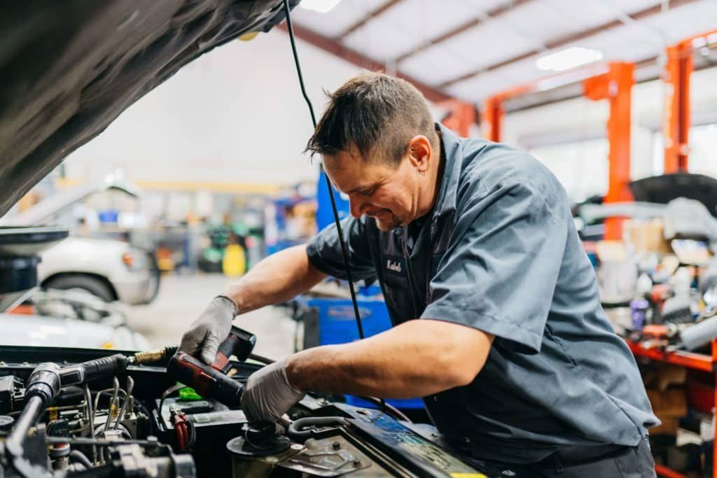 Mechanic working under an open car hood in an auto repair shop