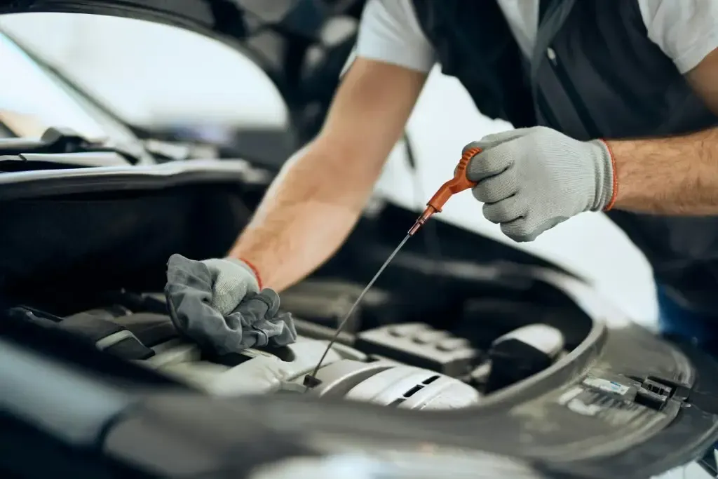Mechanic checking engine oil with a dipstick under an open car hood