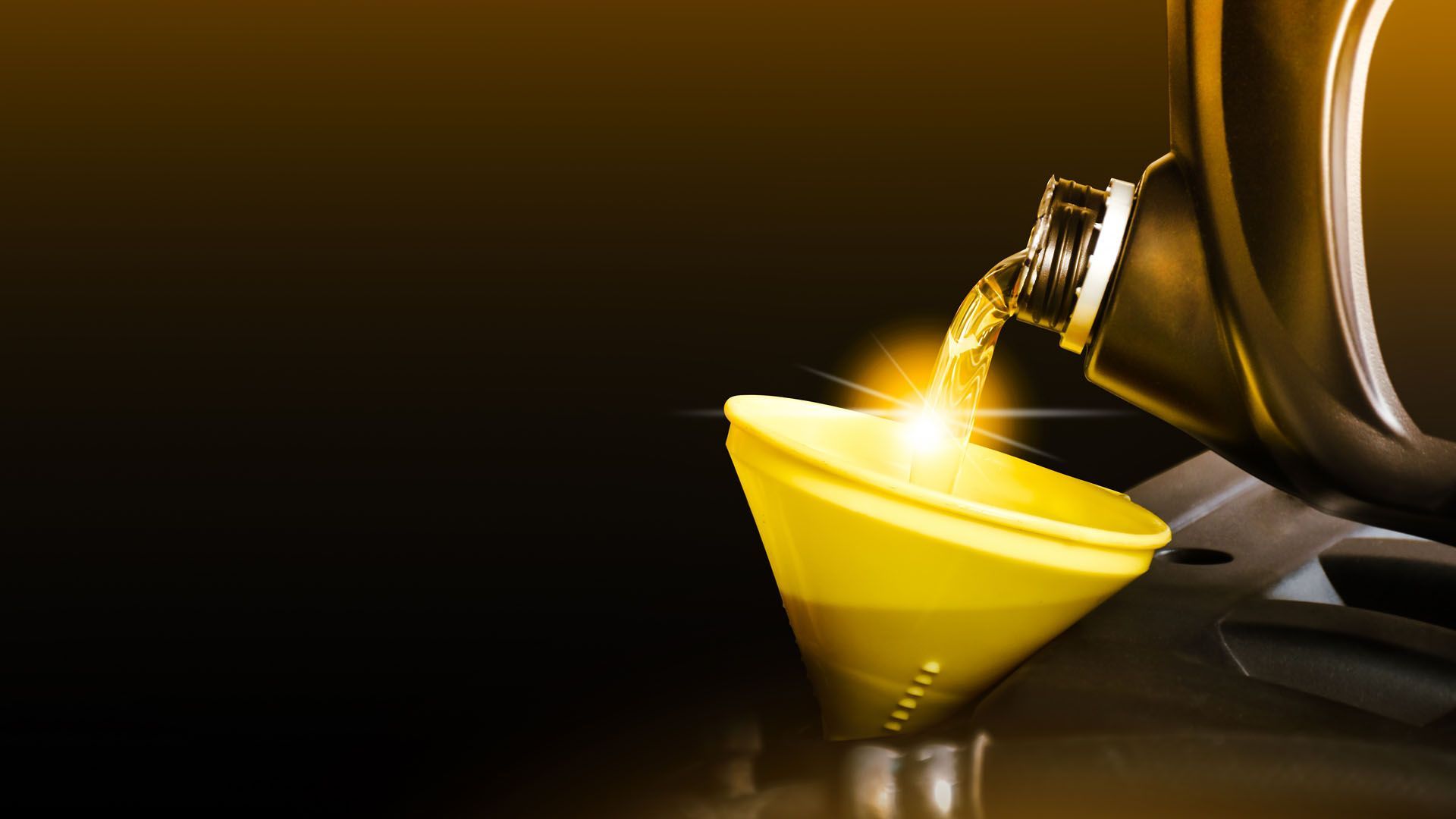Golden olive oil pouring into a small yellow bowl beside a bottle on a dark surface