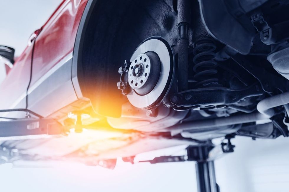 Underside of a red car on a lift, showing a wheel and brake disc with bright workshop light.