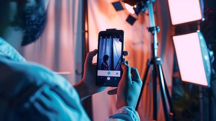 Una persona riprende un set da studio con uno smartphone, incorniciato da luci arancioni e blu.