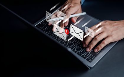 Mani che digitano su un laptop, con icone luminose di buste email sullo schermo