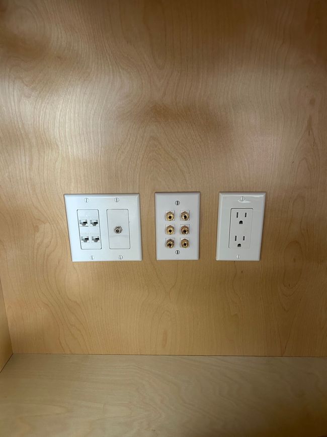 Three wall-mounted outlet and light switch plates on a wood-paneled wall.