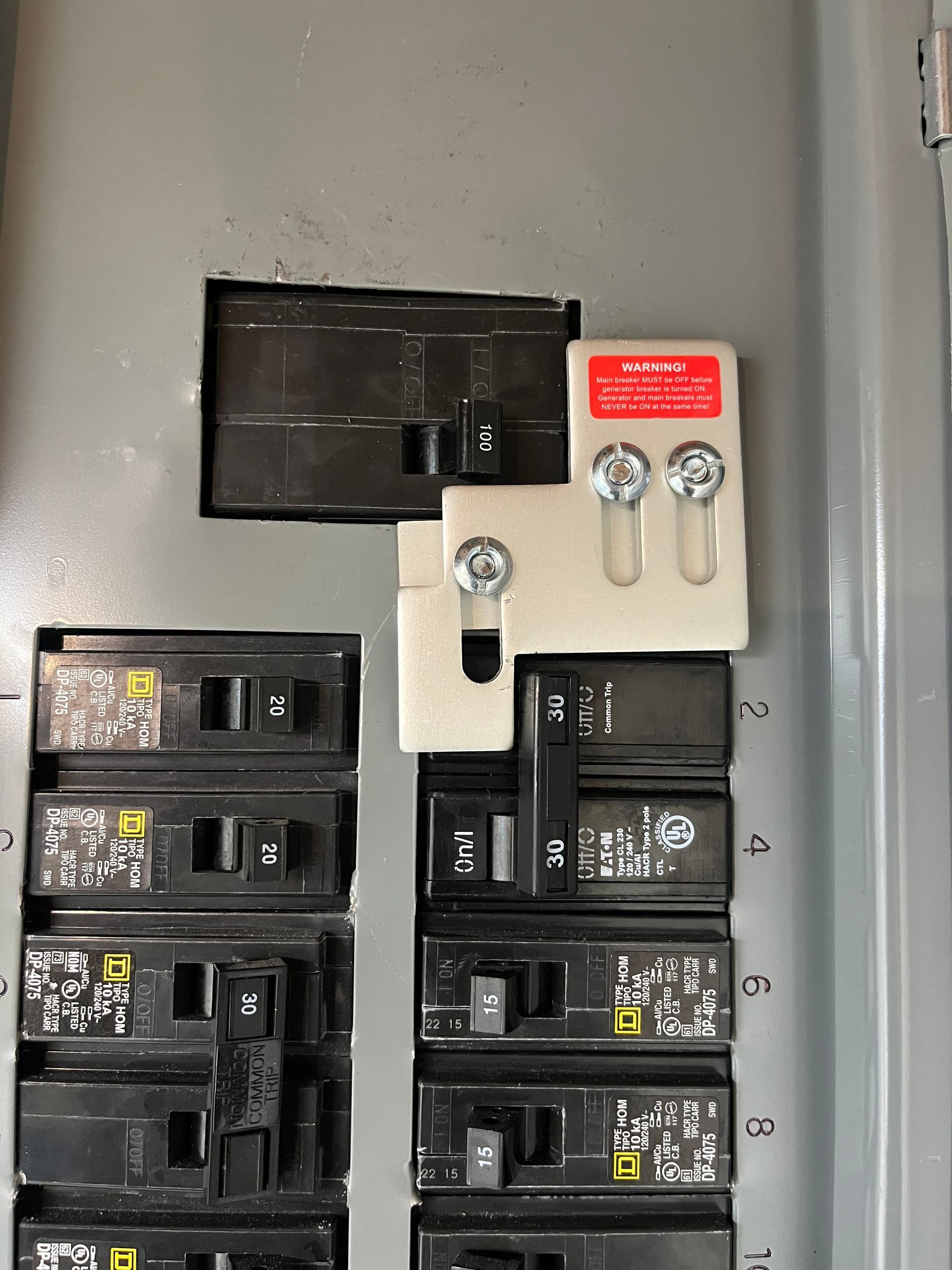 Electrical breaker panel with black circuit breakers and a white meter base on a gray wall.