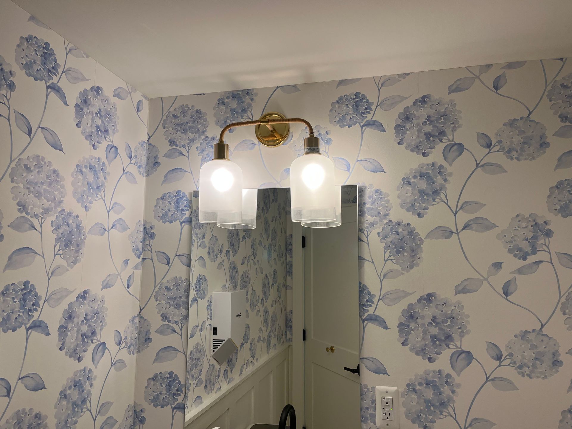Bathroom with blue floral wallpaper, vanity mirror, and two lit pendant lights.