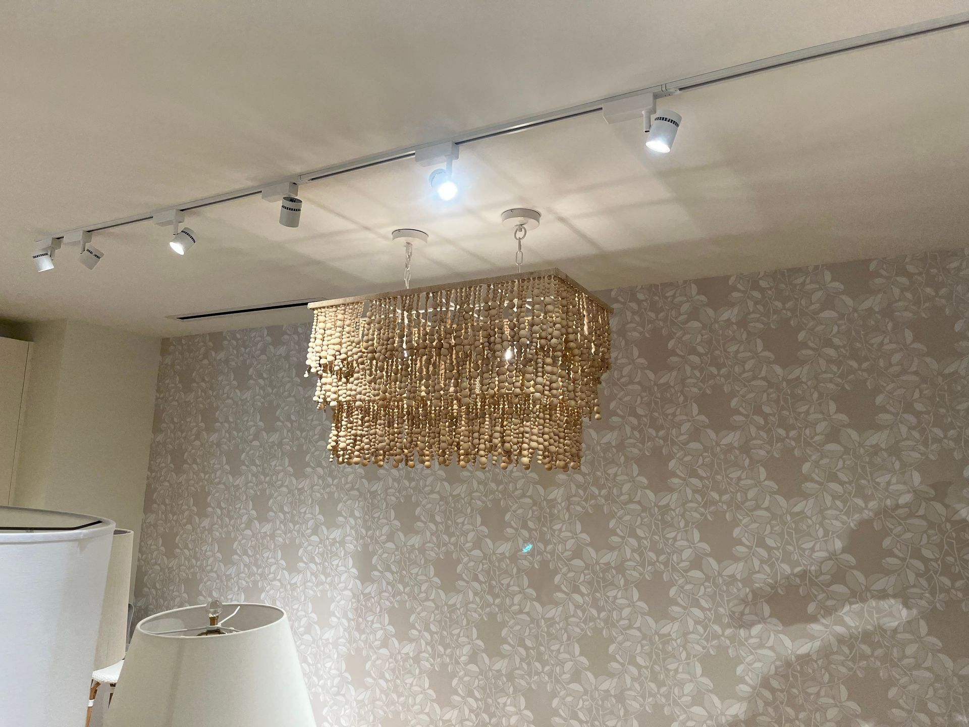 Gold chandelier hanging from a white ceiling in a room with patterned wallpaper and track lighting.