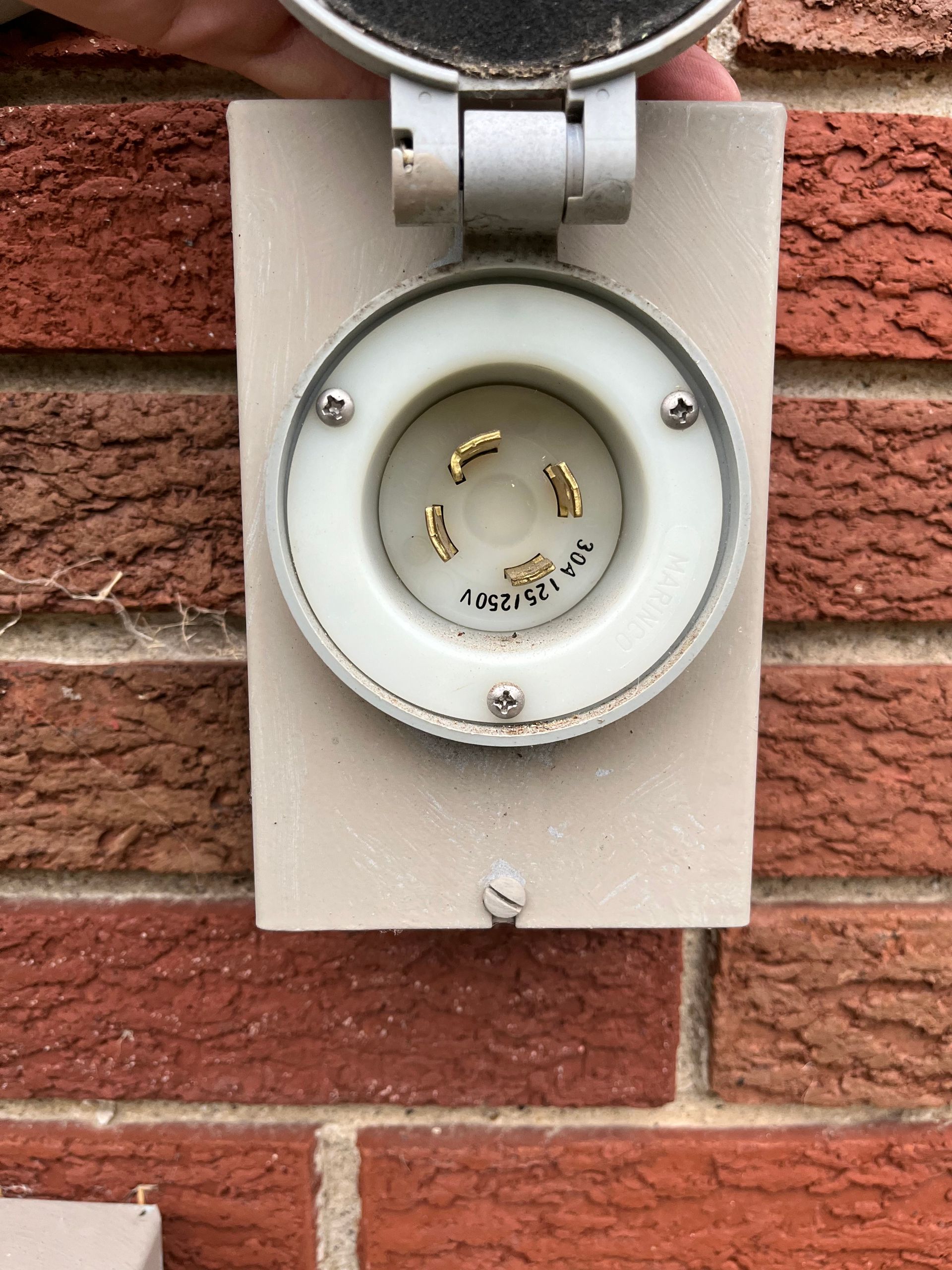 Round white electrical outlet on a brick wall, with cover open and no plug inserted.