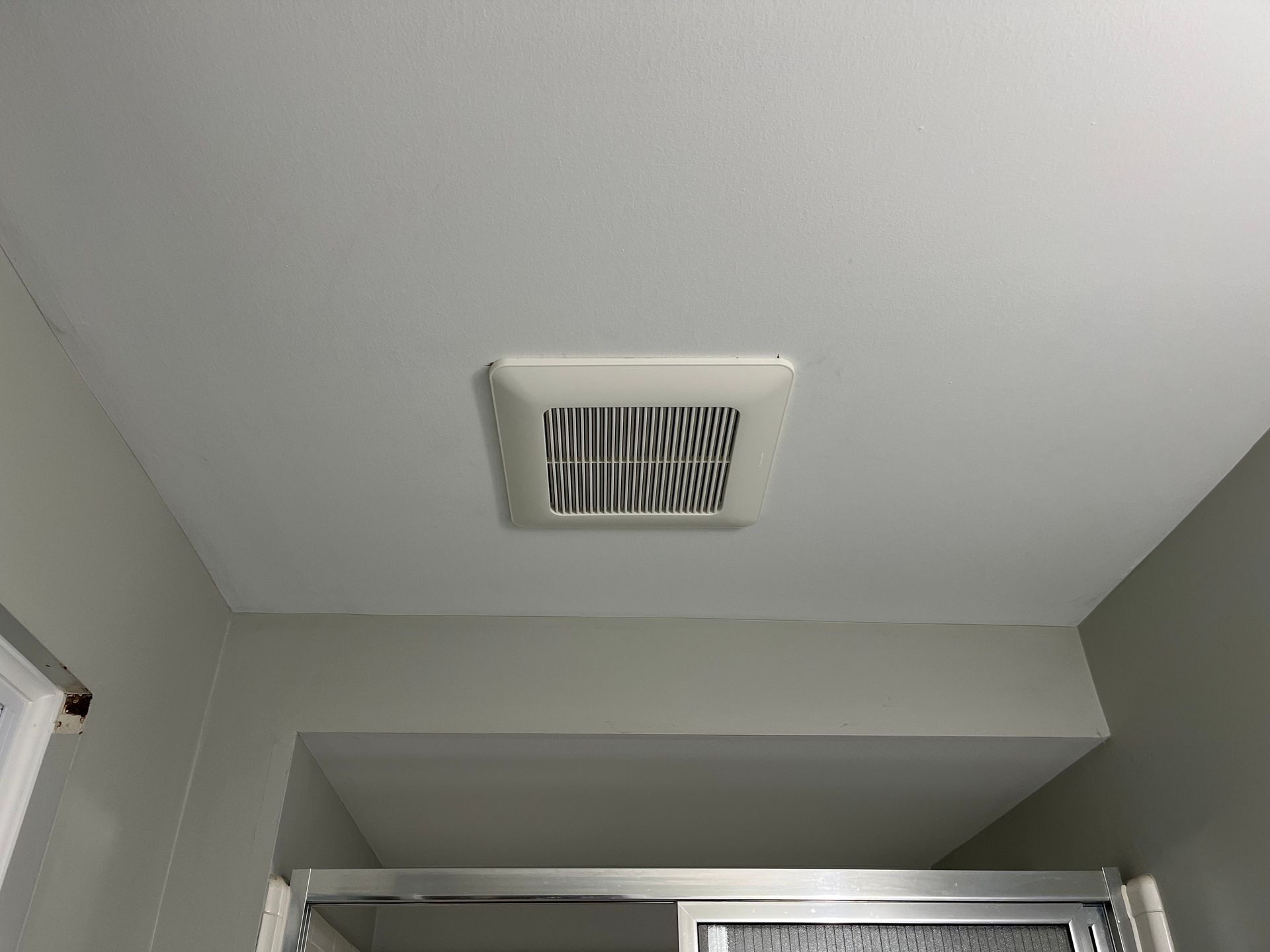 Bathroom ceiling with a white vent above a shower curtain rod