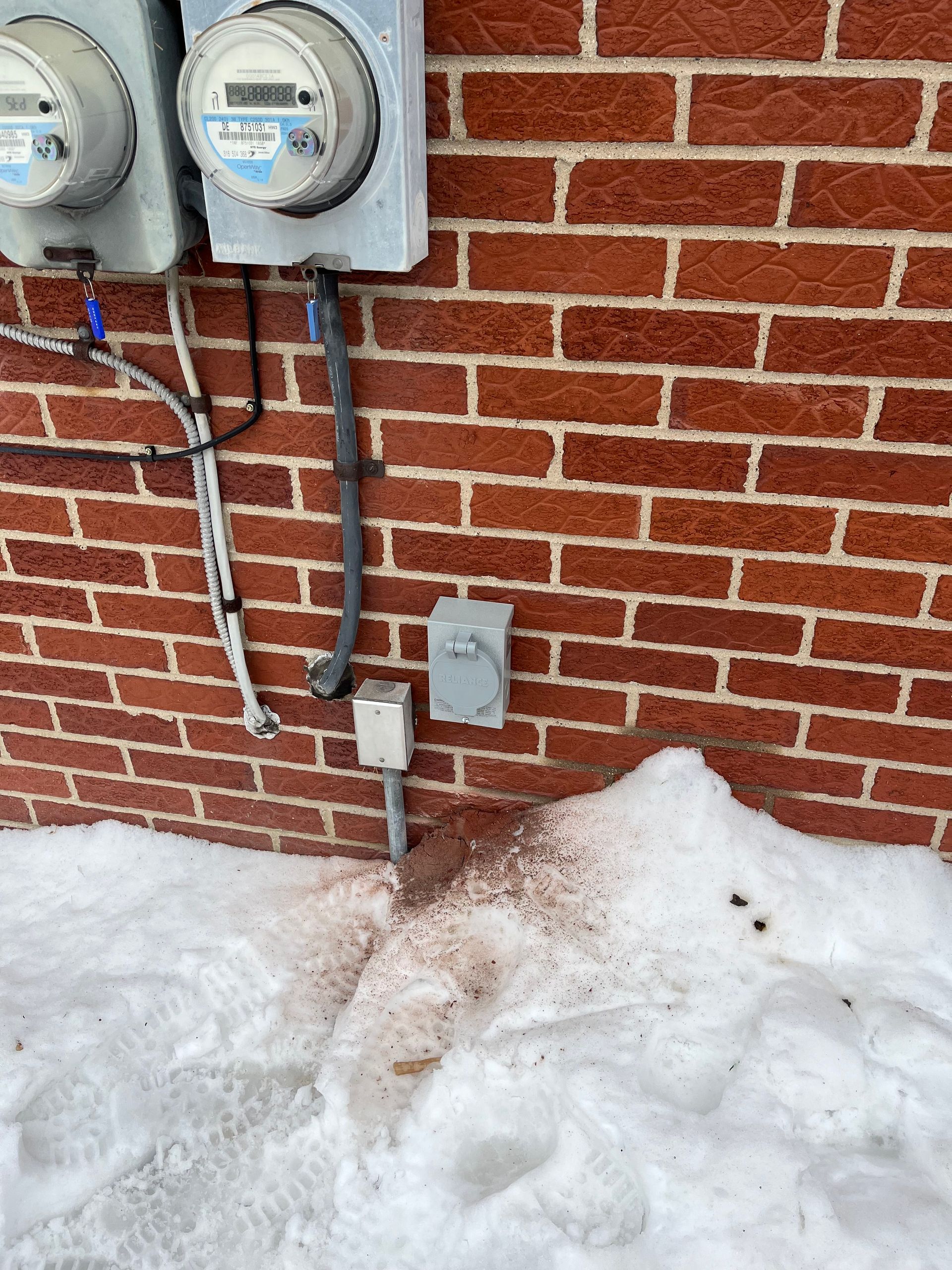 Two electric meters and conduit on a brick wall above a snowbank