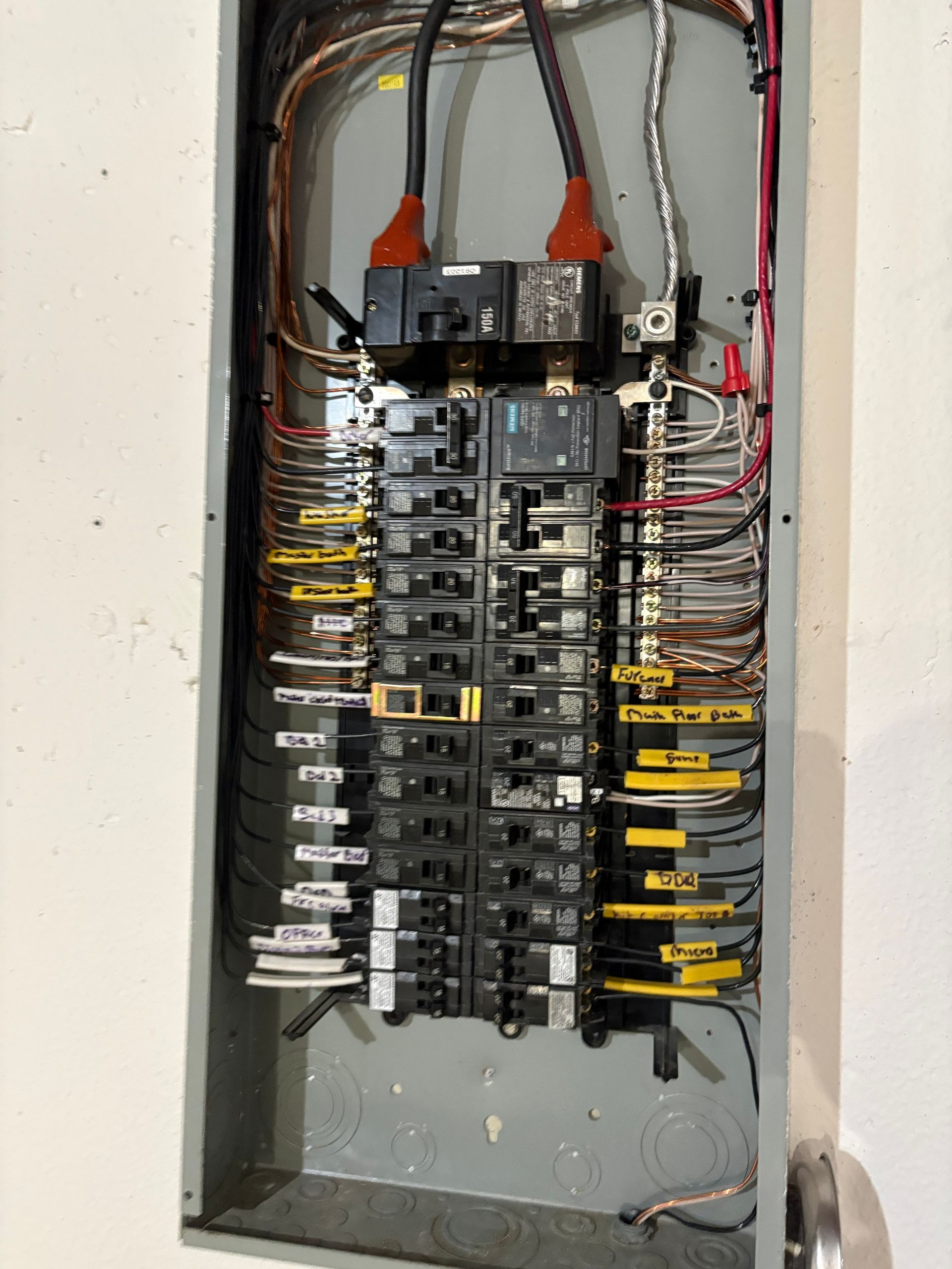 Open electrical breaker panel with wires and circuit breakers in a wall recess