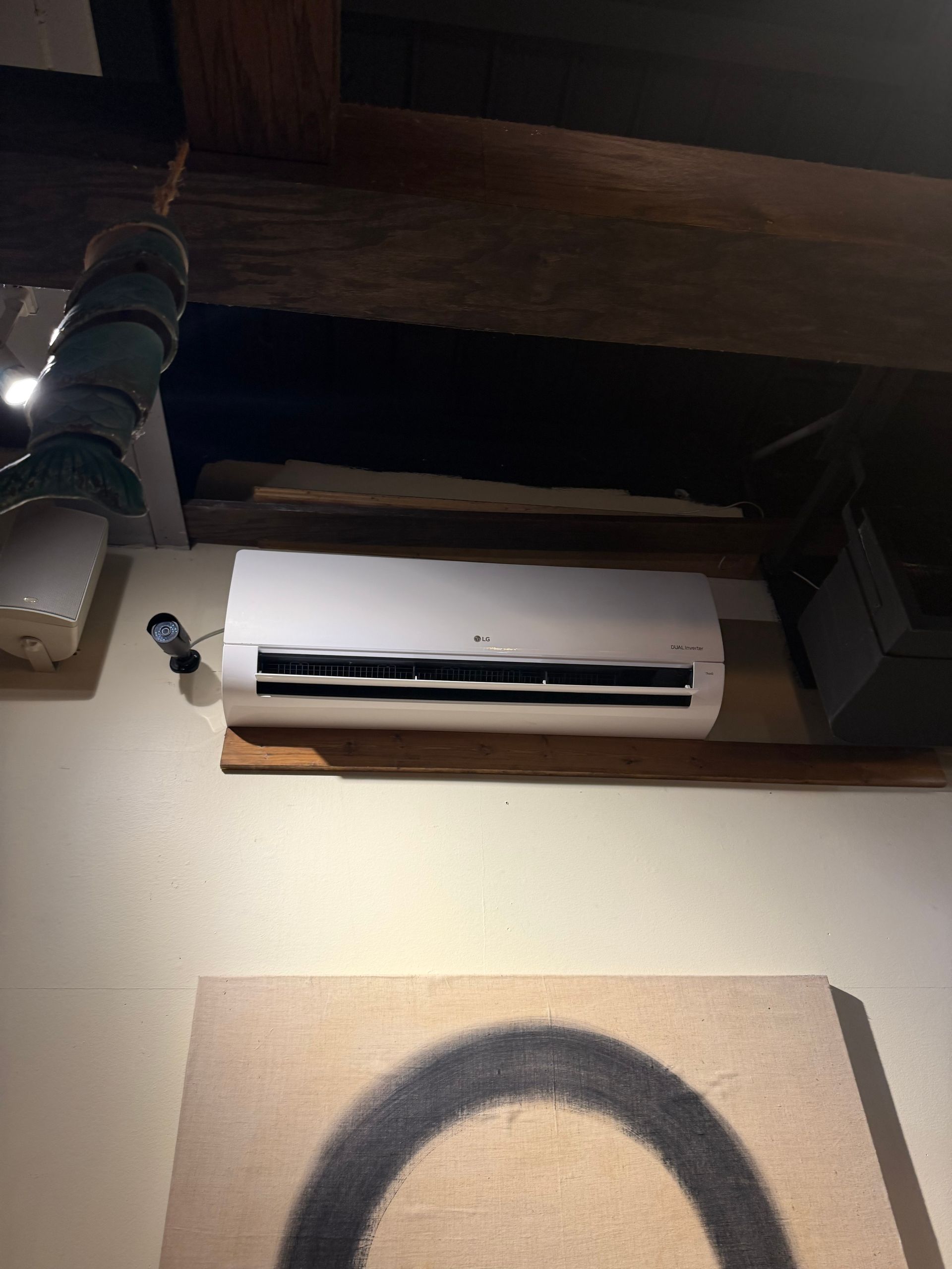 Wall-mounted white air conditioner above a framed black arc artwork on a beige wall.