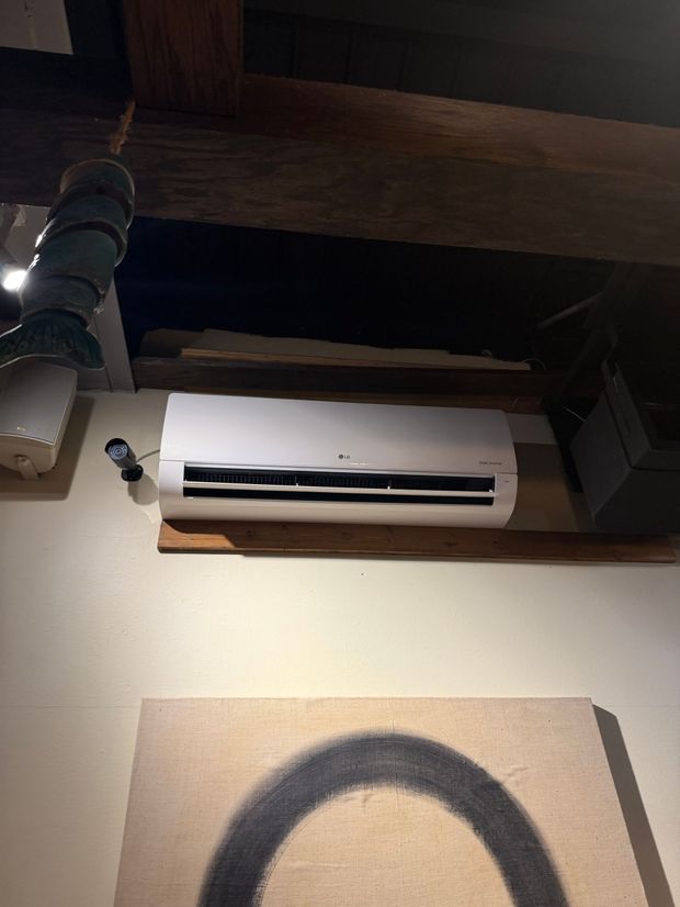 Wall-mounted white air conditioner above a framed black arc artwork on a beige wall.