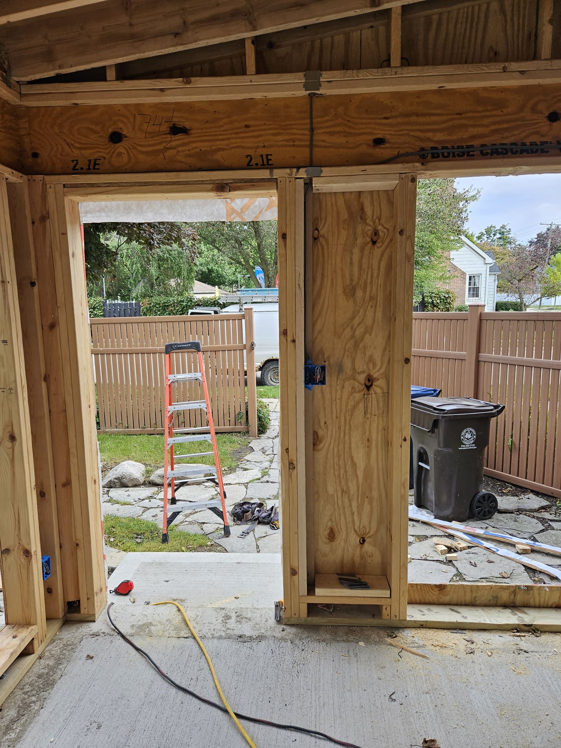Unfinished doorway in a house under construction, with an orange ladder and yard visible outside.