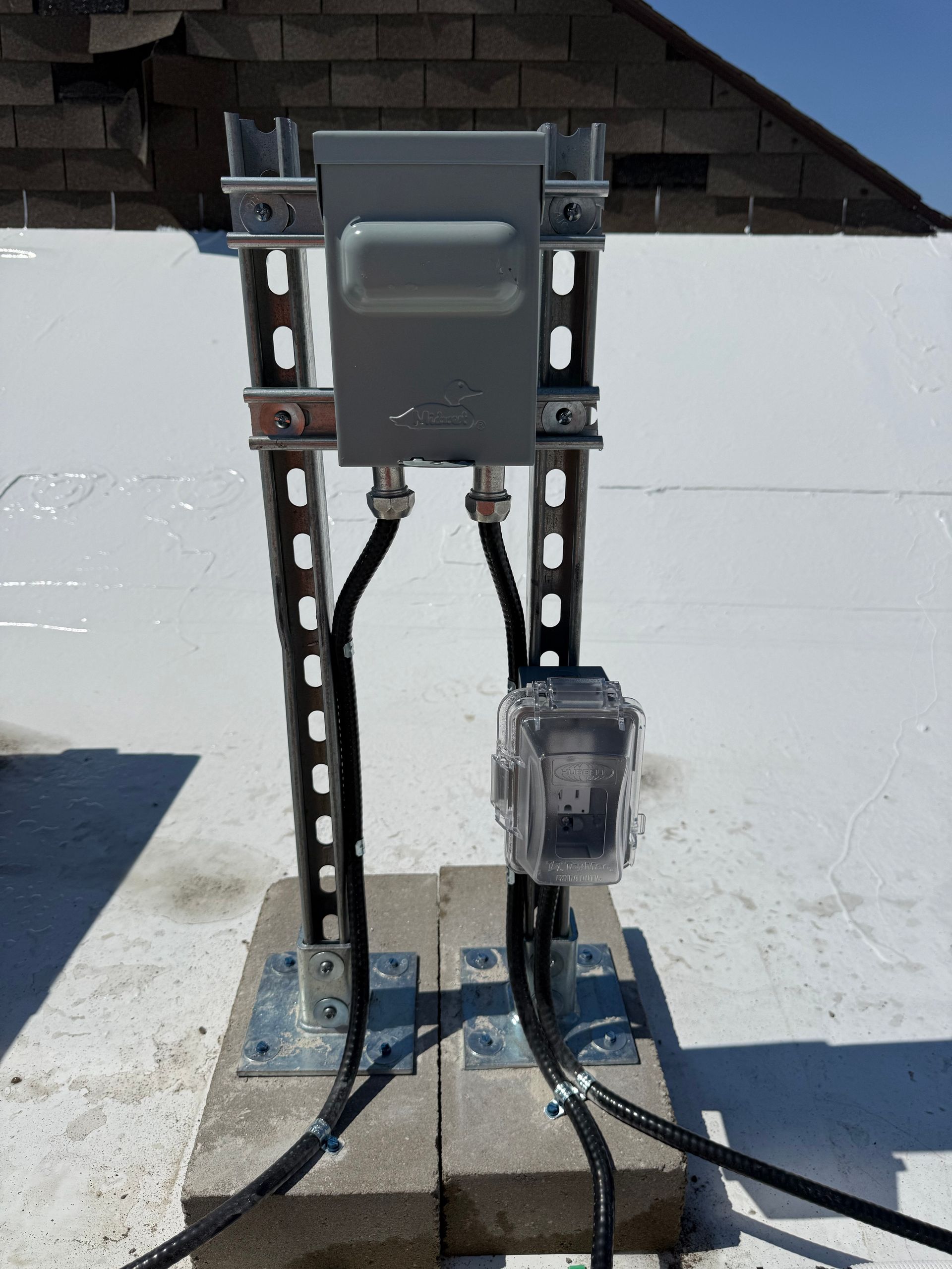 Outdoor electrical meter panel mounted on metal posts with conduit and wiring near a wall