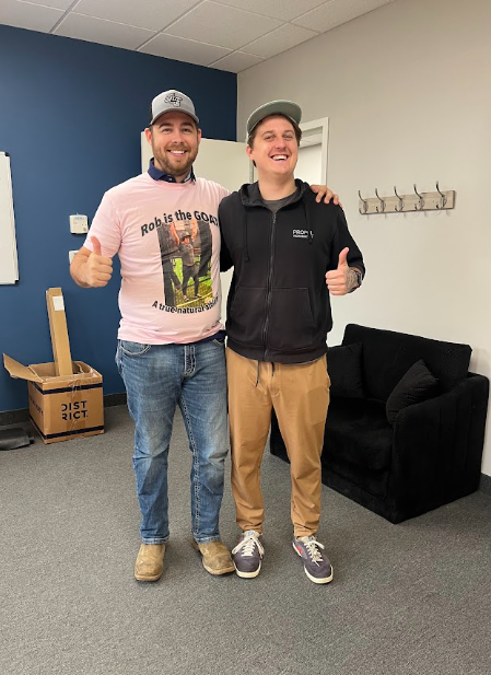 Two smiling people giving thumbs up in an office lounge with blue wall and black couch