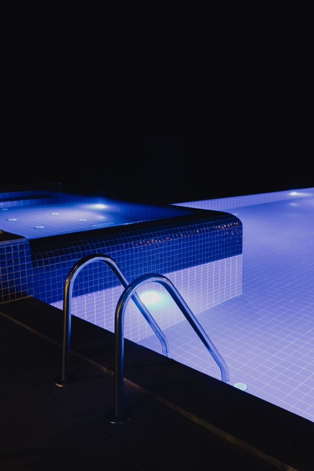 Blue-lit swimming pool with metal ladder at the edge