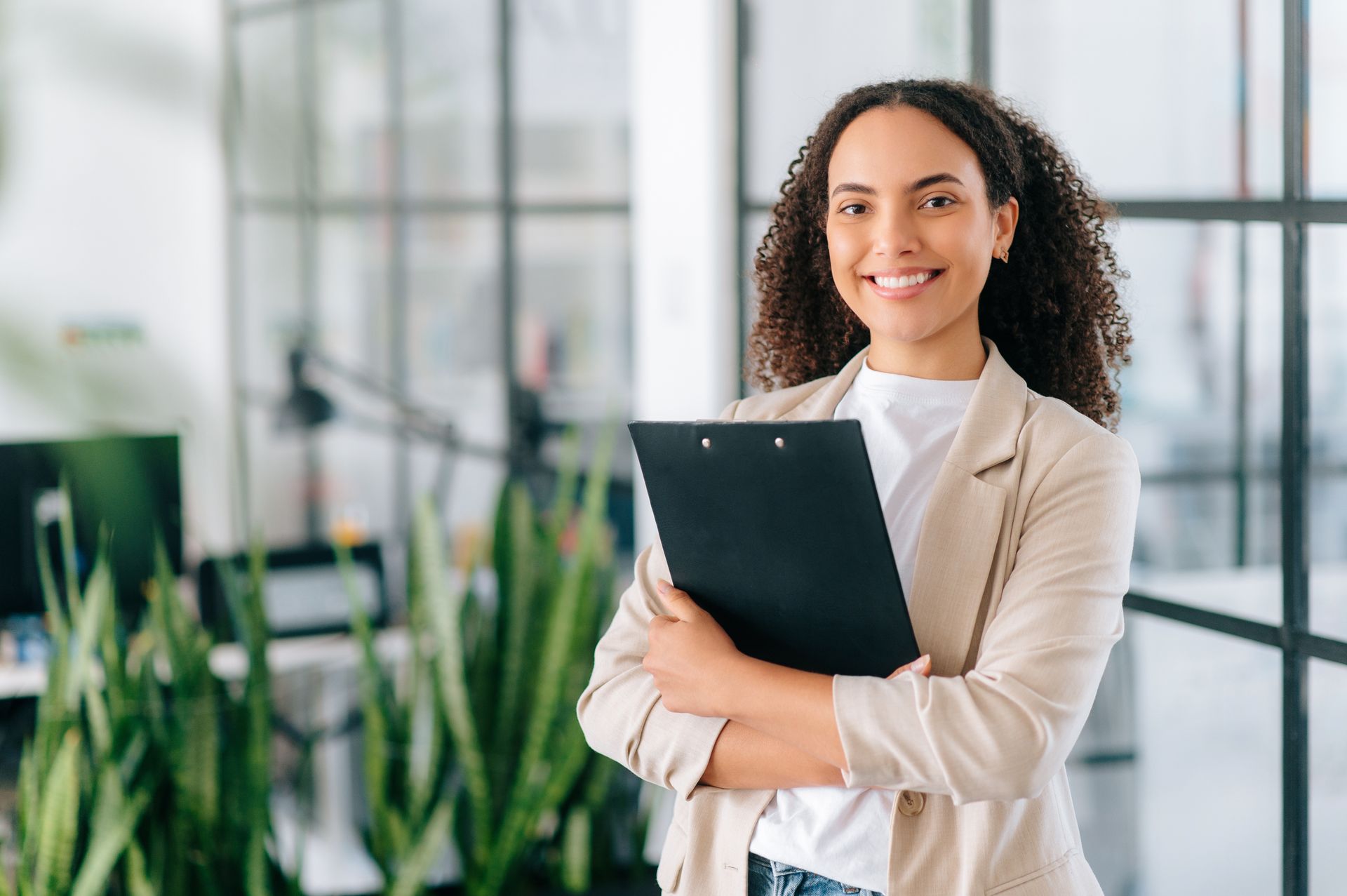 Woman holding a black folder in a modern office, smiling at the camera.