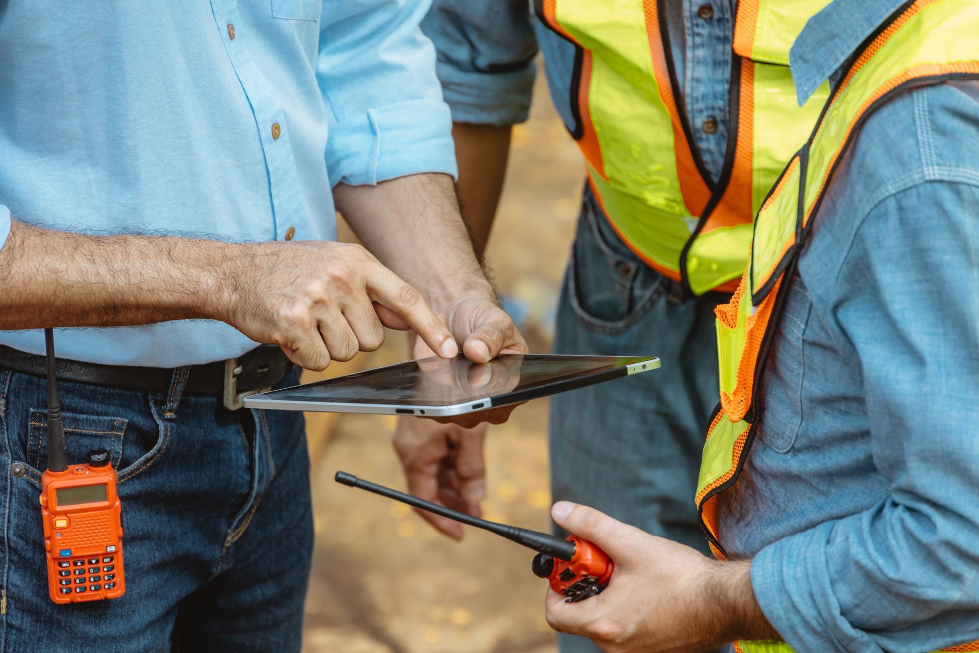 Two workers in safety vests using a tablet and smartphone at a construction site