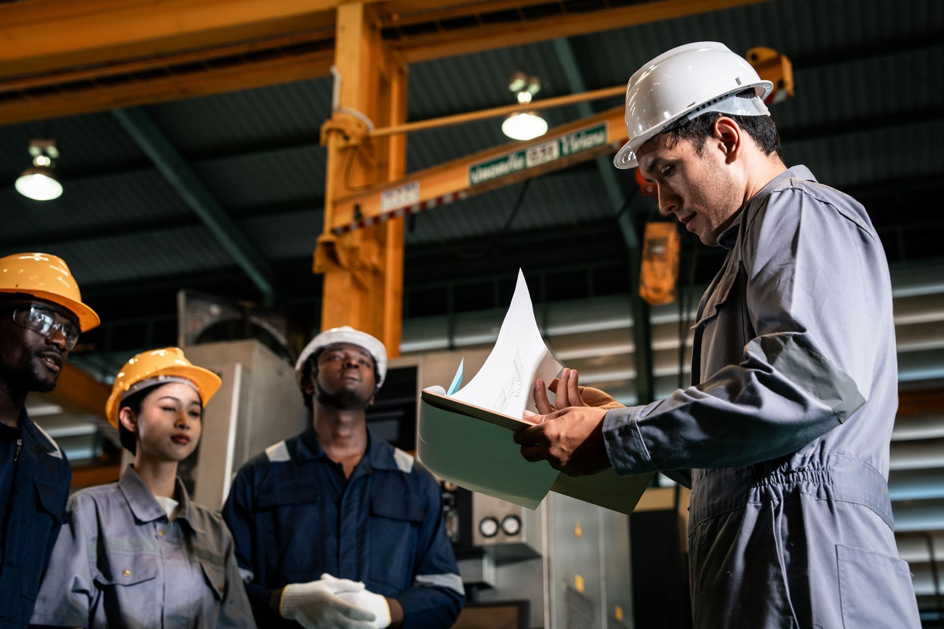 Workers in hard hats review plans together inside an industrial factory.