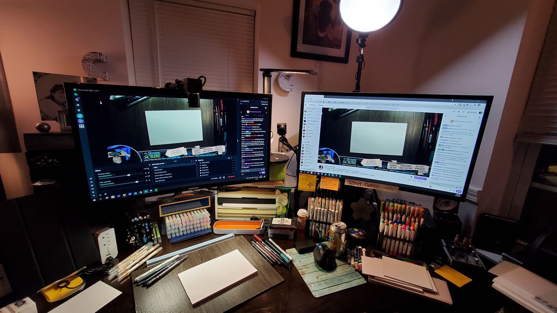 A desk with two monitors and a lamp on it