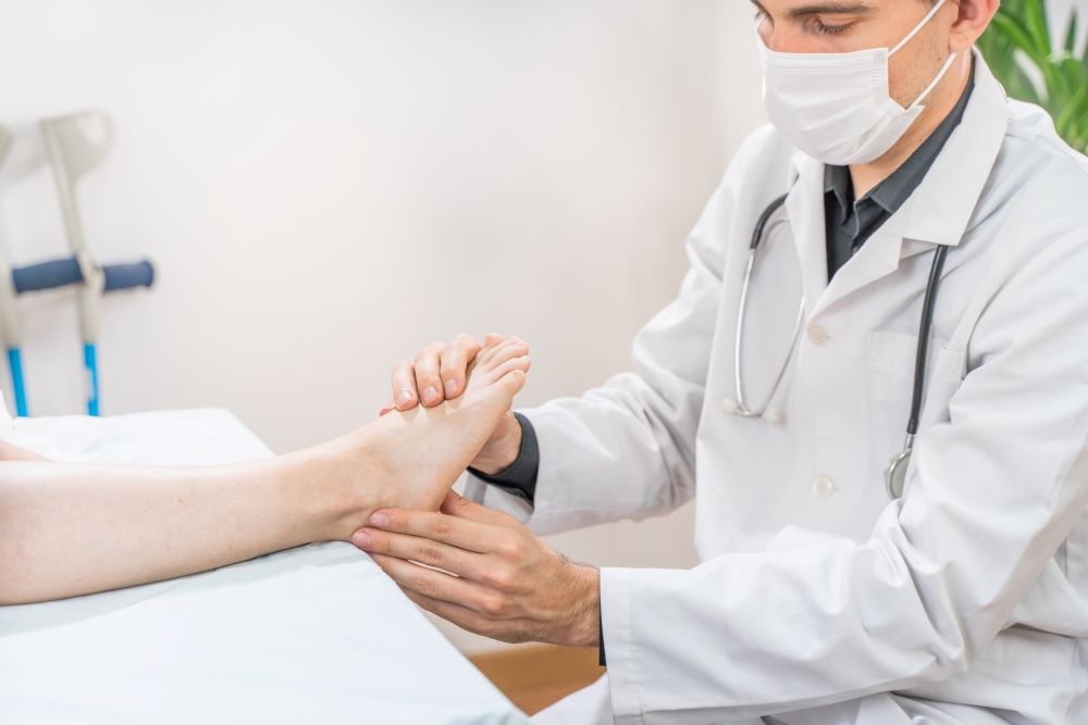 A Doctor Wearing A Mask Is Examining A Patient's Foot — Mooloolaba Foot Centre In Mooloolaba, QLD