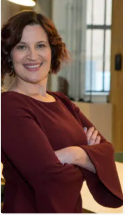 Smiling woman in a burgundy top stands with arms crossed in a bright indoor office setting