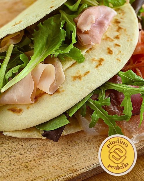 Piadina ripiena di verdure e prosciutto su un tagliere di legno.