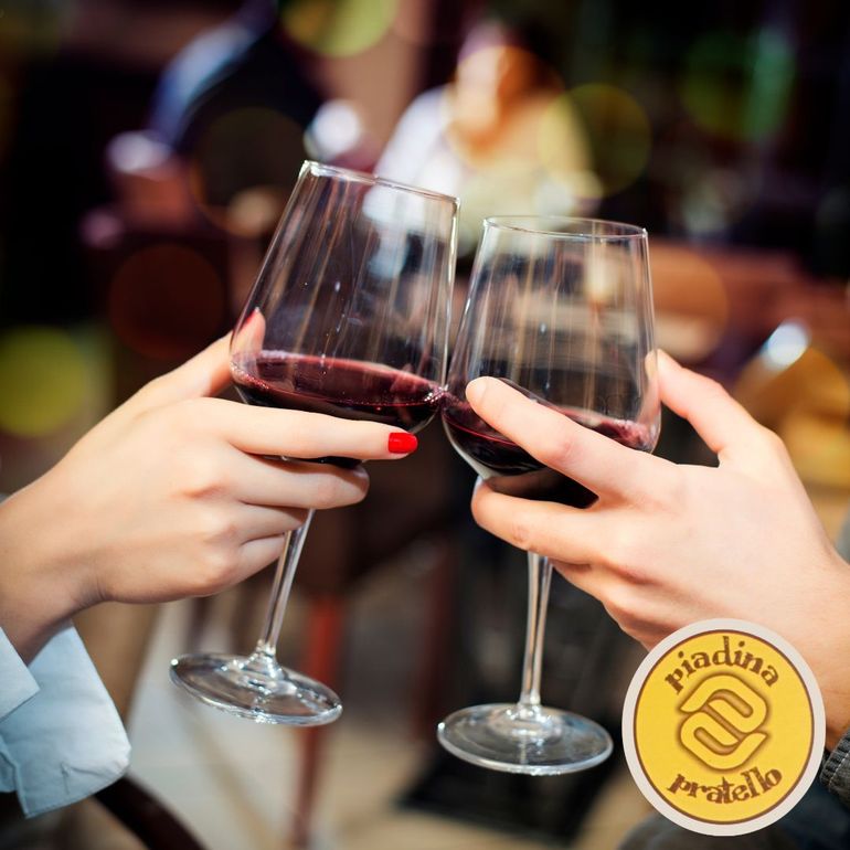 Mani che alzano calici di vino rosso in un brindisi a un tavolo di un ristorante illuminato da luci soffuse.