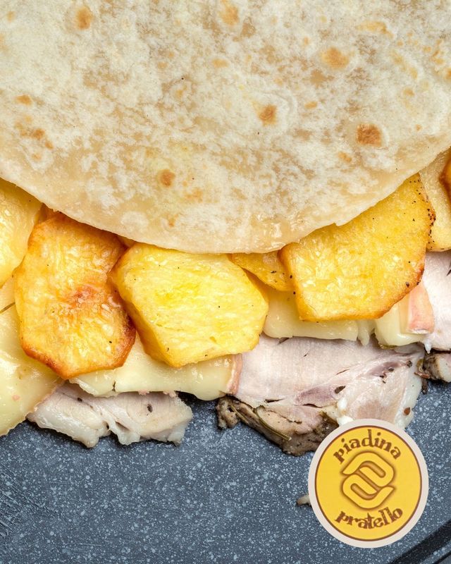 Primo piano di un panino pita con fette di patate fritte dorate e ripieno di carne su una superficie scura.