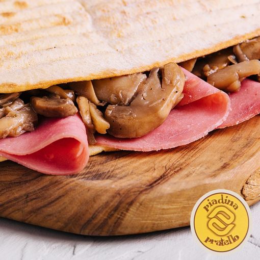 Primo piano di un panino piegato con prosciutto rosa e funghi su un tagliere di legno.