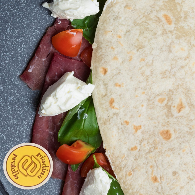Piadina ripiena di lattuga, pomodoro, formaggio e carne a fette, servita su un piatto scuro.